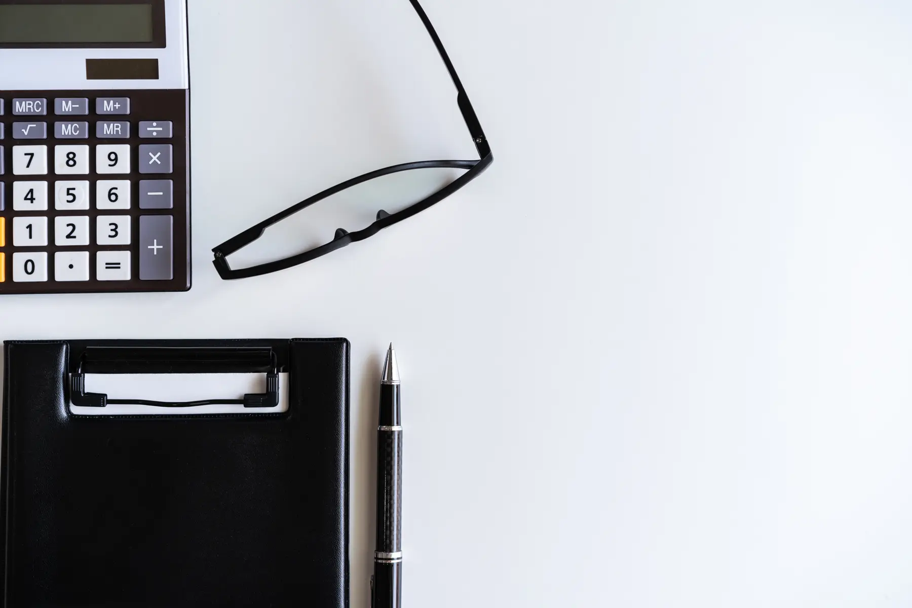 A calculator, a clipboard and glasses on a white desk